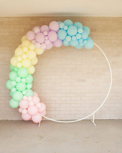 Pastel rainbow balloon garland arch with soft colors against a textured wall, creating a festive atmosphere.