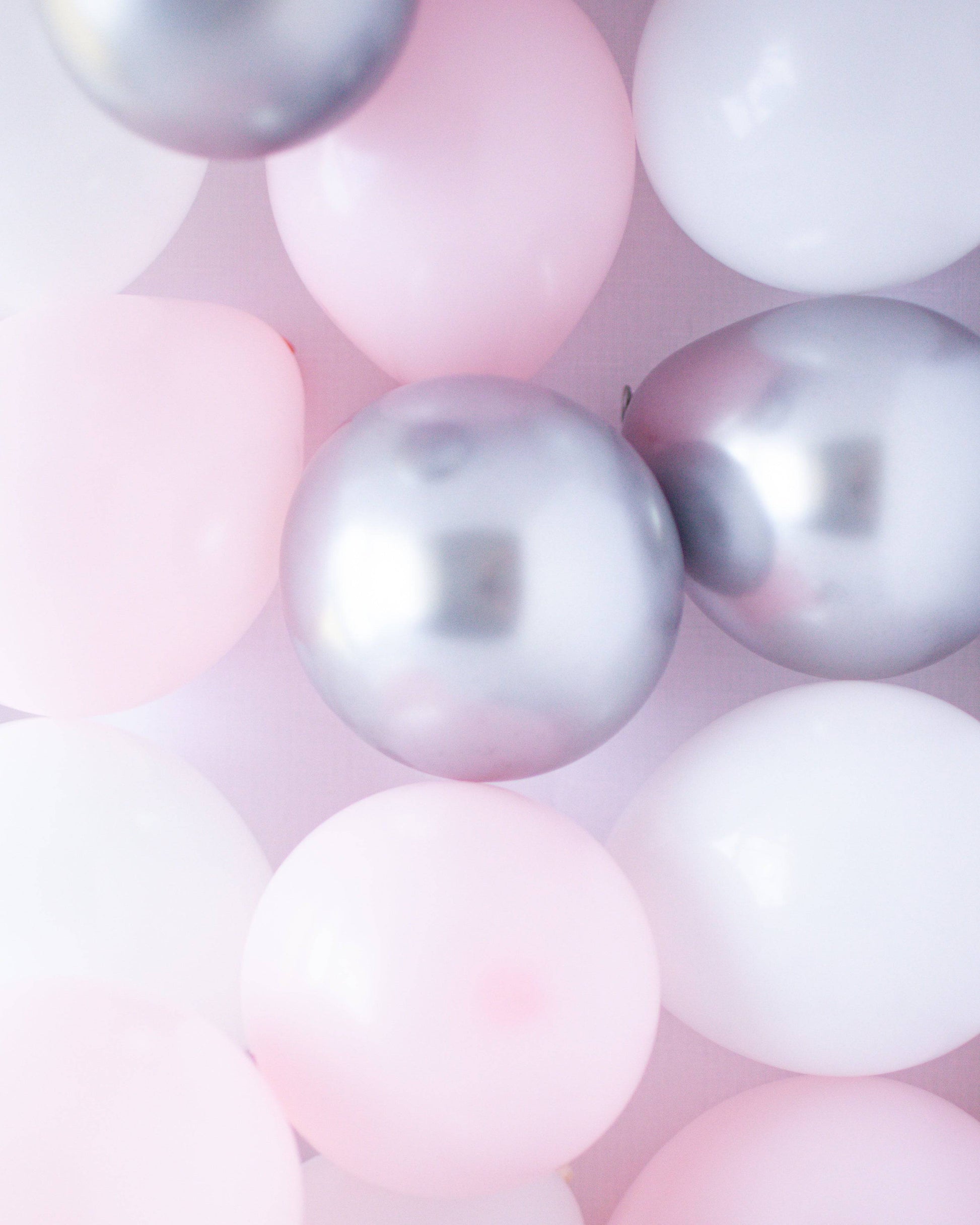 A mix of pink, white, and silver balloons scattered against a soft background, creating a festive atmosphere.