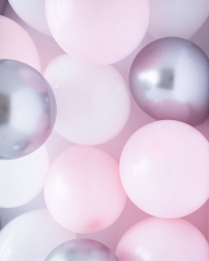 A colorful mix of pink, white, and silver balloons in various sizes, creating a cheerful and festive atmosphere.