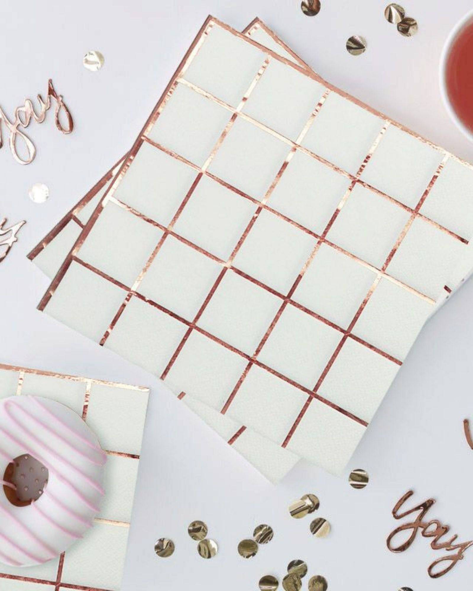 Rose gold checkered napkins arranged with a frosted donut and scattered confetti on a light surface.