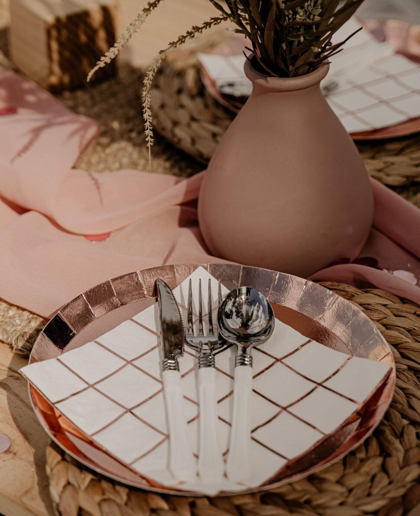 Rose gold checkered napkins on a plate with silver utensils, set against a natural, textured background.