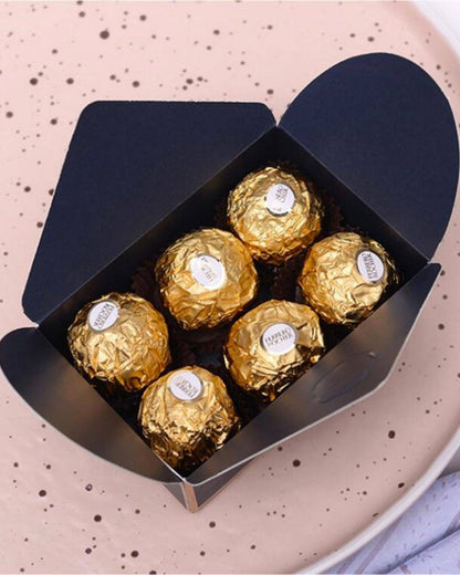 Navy blue favor box containing six golden, round treats, set against a soft, speckled background.