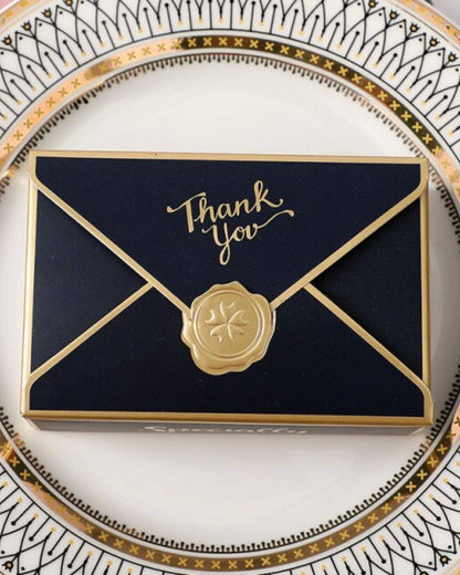 Elegant navy box with gold accents and "Thank You" script, resting on a decorative plate with intricate patterns.