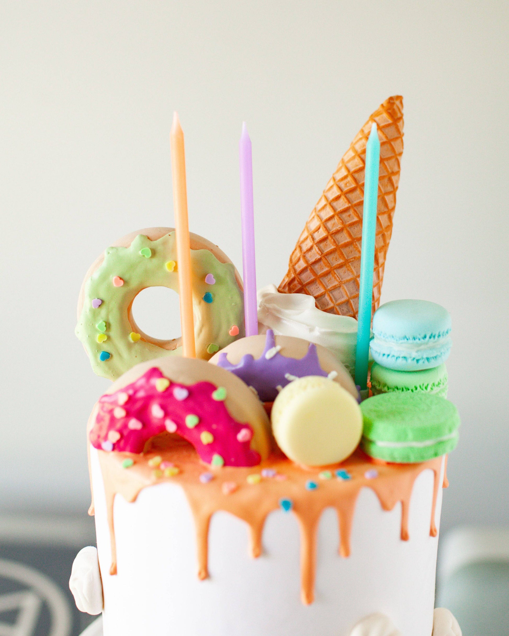 Colorful candles atop a cake, surrounded by vibrant donuts, macarons, and an ice cream cone.