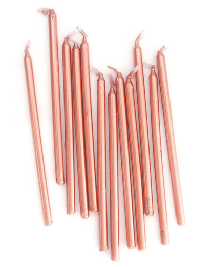 A cluster of tall, rose gold candles with pointed tips, arranged on a light background.