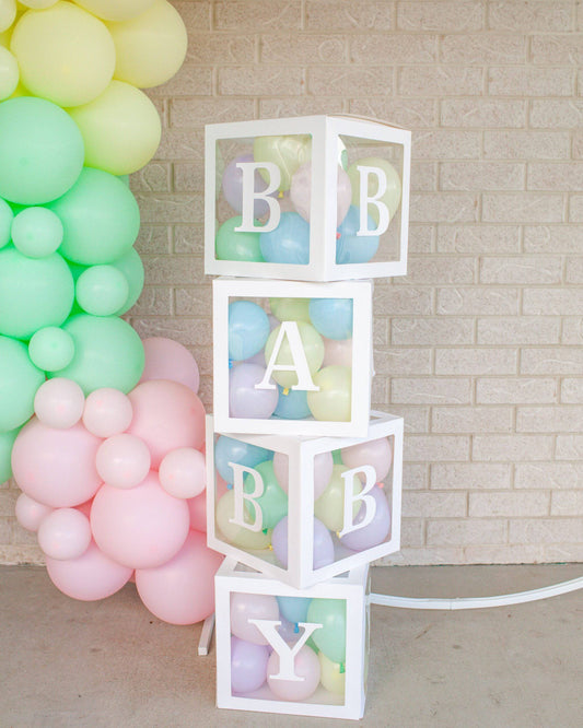 Four transparent boxes stacked with pastel balloons inside, spelling "BABY" against a soft balloon backdrop.