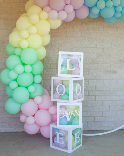 Colorful balloons in pastel shades form an arch, with clear boxes spelling "LOVE" stacked beside them.