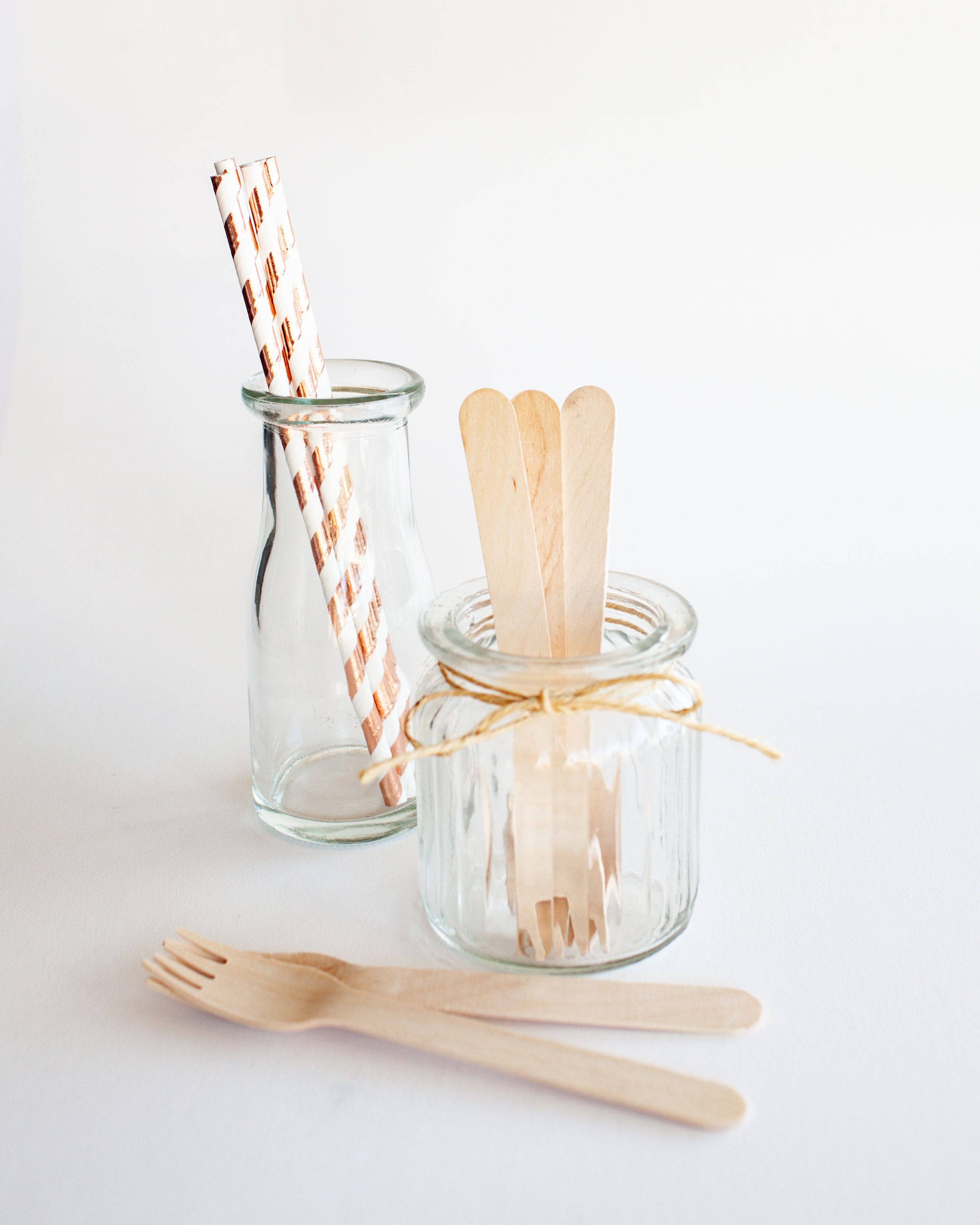 A collection of wooden forks and straws displayed in glass jars with twine accents on a light background.